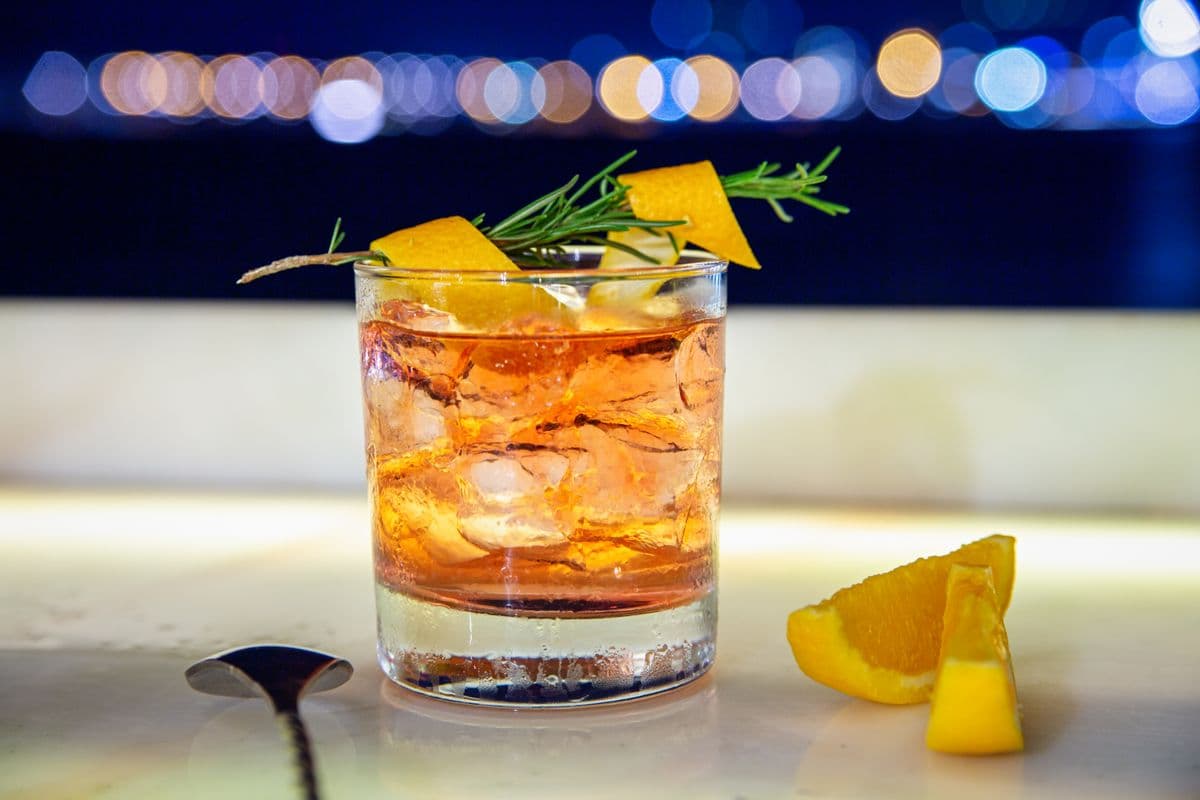 A craft cocktail garnished with rosemary and orange.