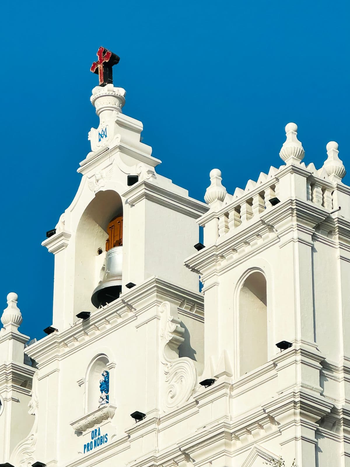 A white Goan church tower against a deep blue sky.