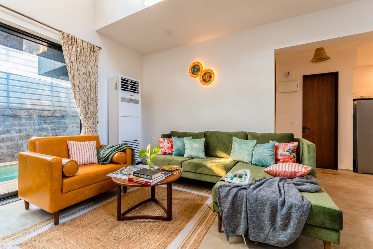 A Nistula villa sitting room with a green sofa and a glimpse of the pool through the window.