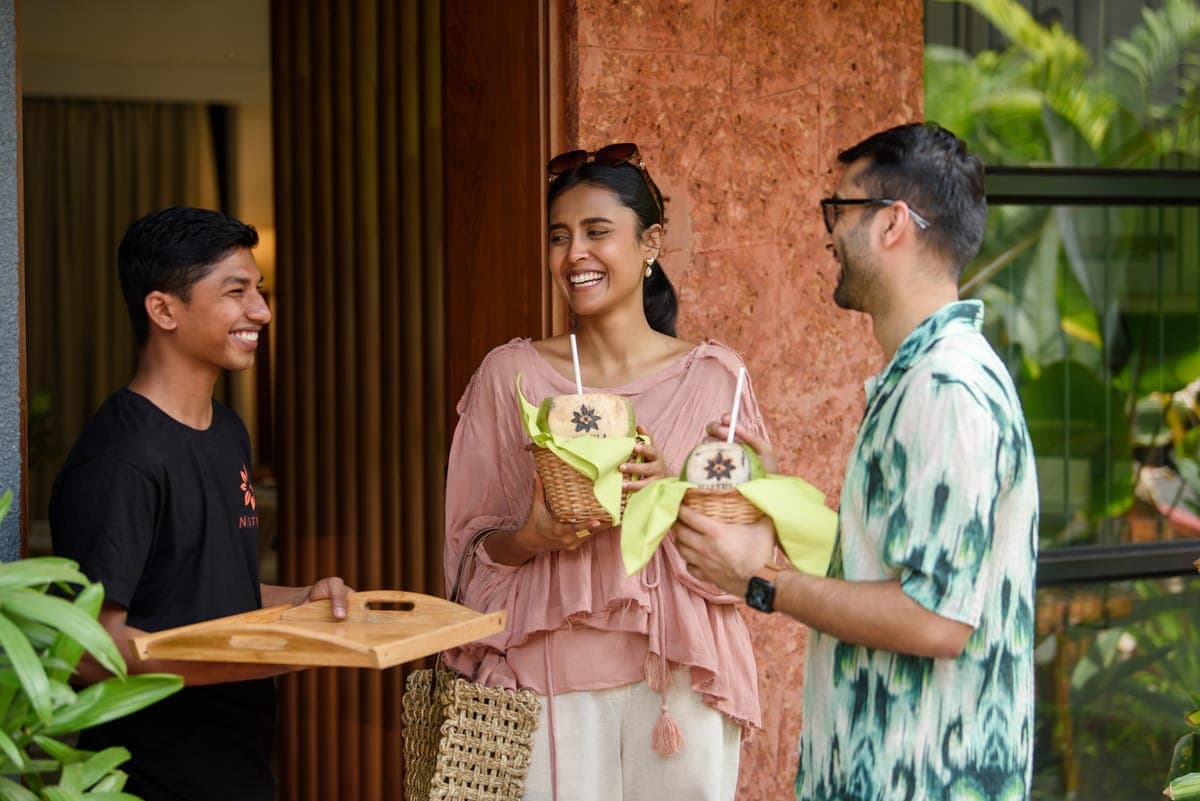 A Nistula host welcoming guests with fresh coconut drinks at the villa door.