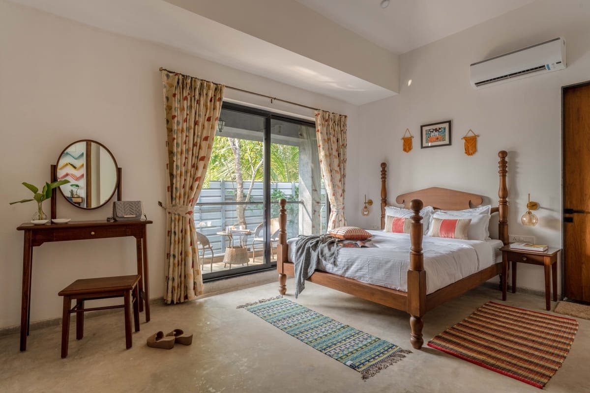 A Nistula villa bedroom with a four-poster bed and sliding doors onto a tree-shaded balcony.