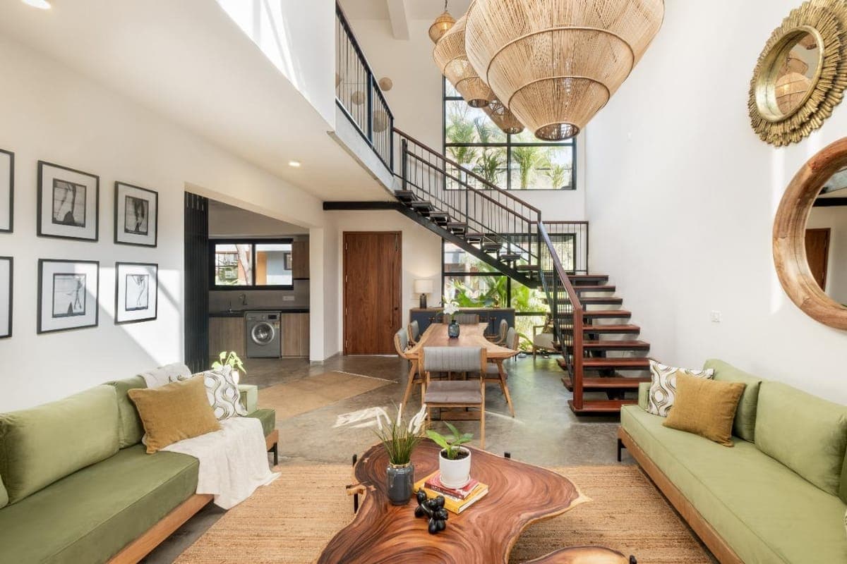 A bright double-height Nistula villa lounge with green sofas and woven pendant lights.